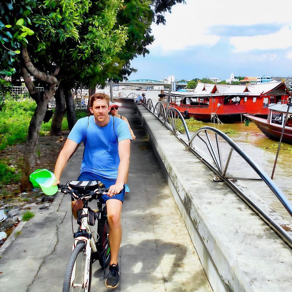 Cyclists riding along a riverside cycle path beside the Chao Phraya River in Bangkok