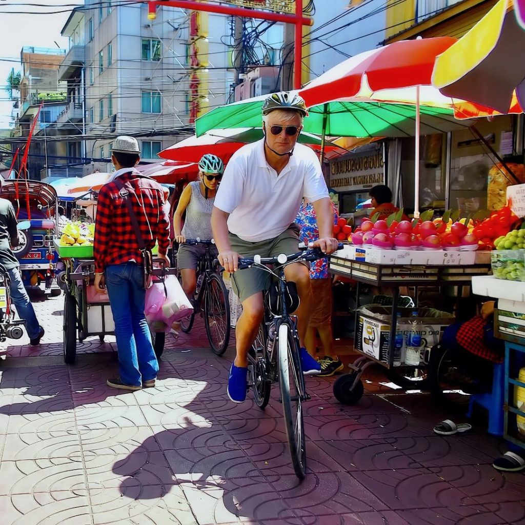 Cyclists riding through a street market in Chinatown, Bangkok