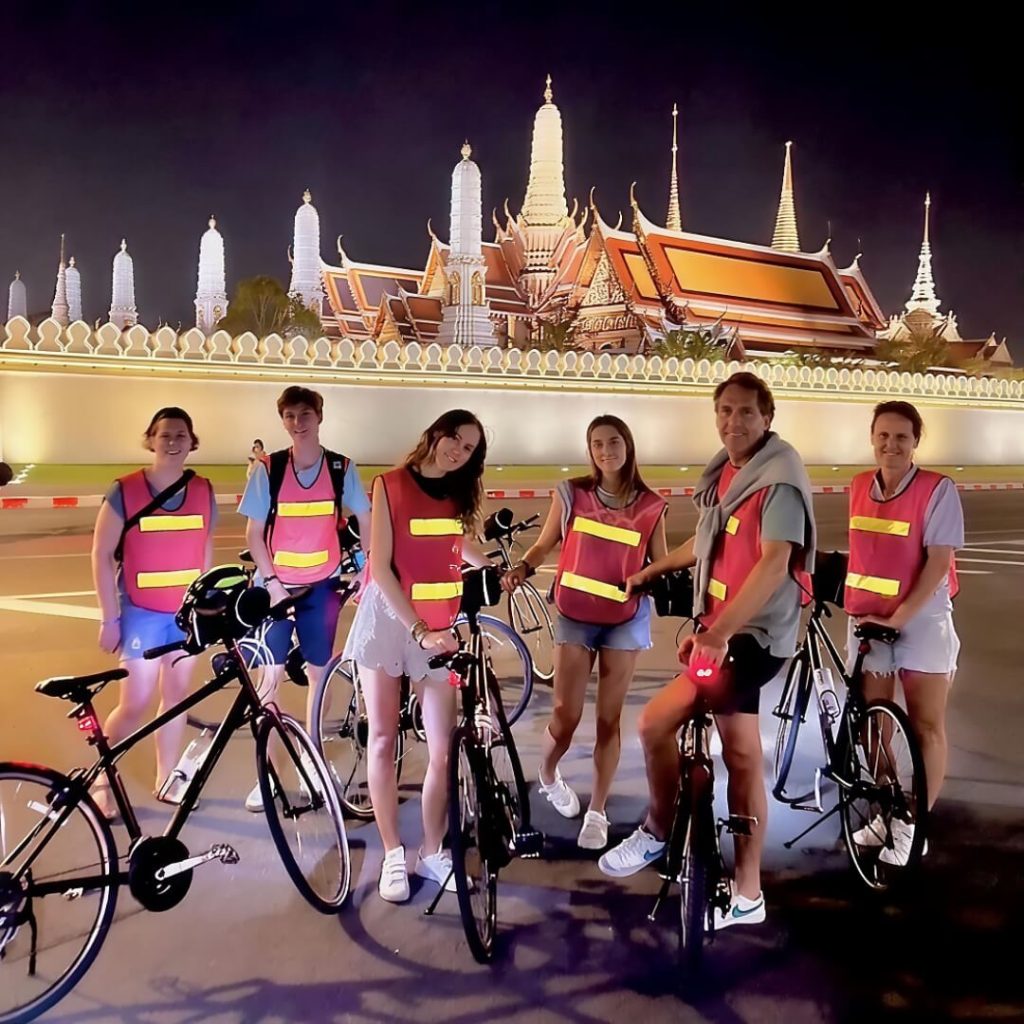 Cyclists standing outside the Grand Palace at night in Bangkok