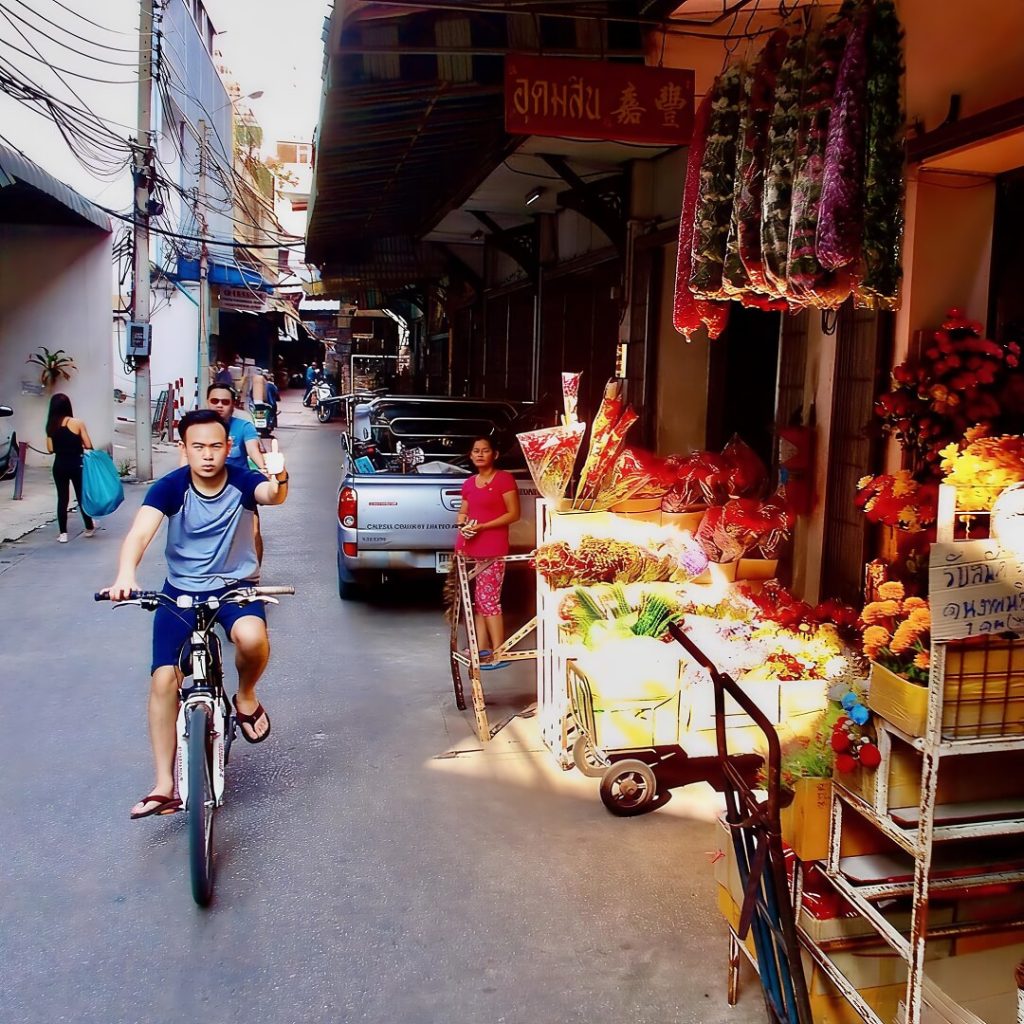 Cyclists riding past flower stalls on a street near Pak Khlong Talat in Bangkok