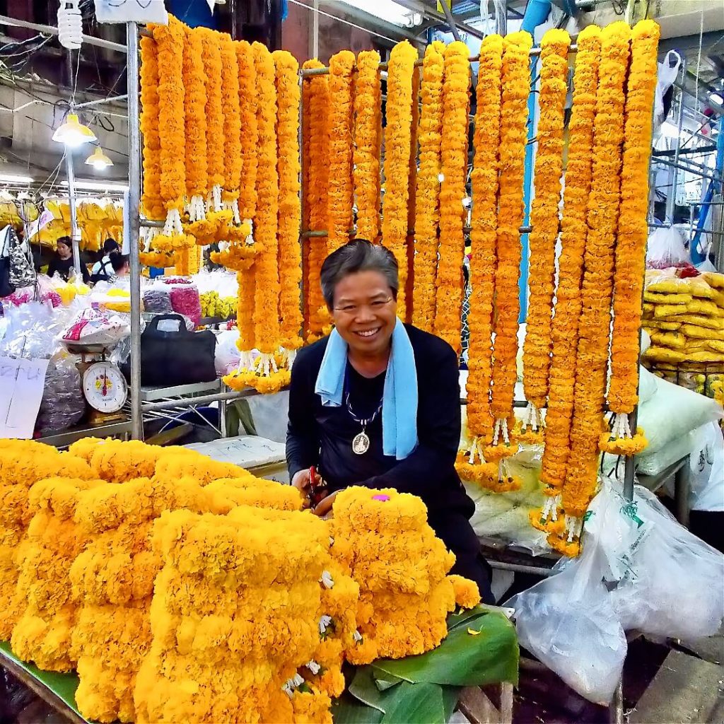 Vendor smiling beside marigold garlands at Pak Khlong Talat Flower Market in Bangkok