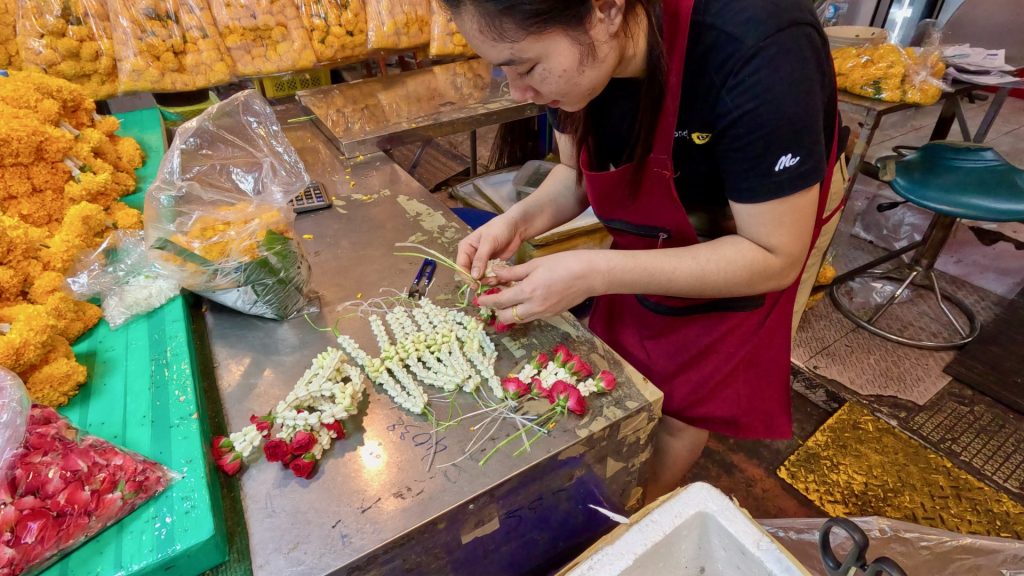 A young girl making garlands from Crown Flowers