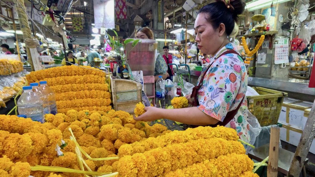 A market vendor creating marigold garlands at the flower market