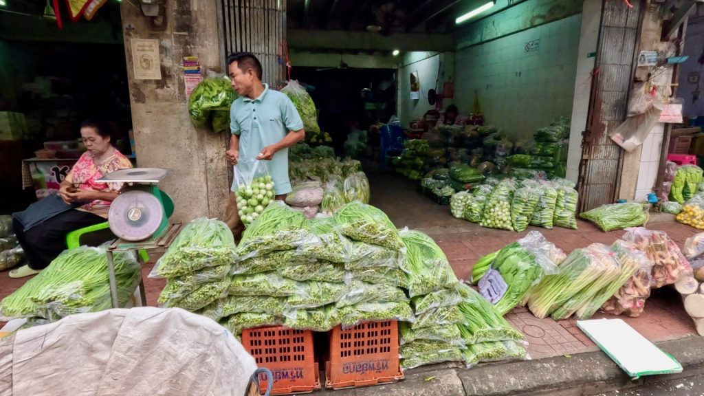 Market vendor packing and selling fresh produce in a Pak Khlong Talad side street