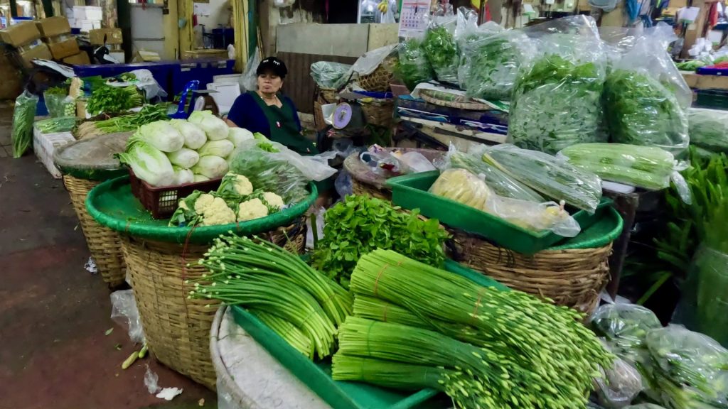 Market vendor relaxing after a busy morning  inside Pak Khlong Talat market, surrounded by her produce for sale
