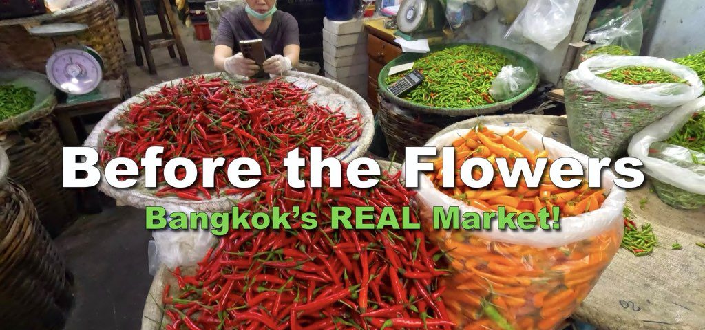 Vendor sitting behind res, green and orange cillies at Pak Khlong Talat-Bangkok Fresh Market