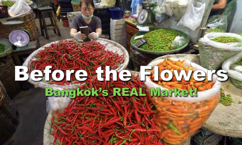 Vendor sitting behind res, green and orange cillies at Pak Khlong Talat-Bangkok Fresh Market