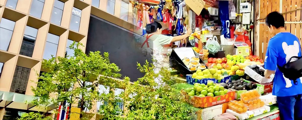 Split view of Silom in Bangkok with office tower on one side and street market vendors on the other during a walk from Sala Daeng to Chong Nonsi BTS