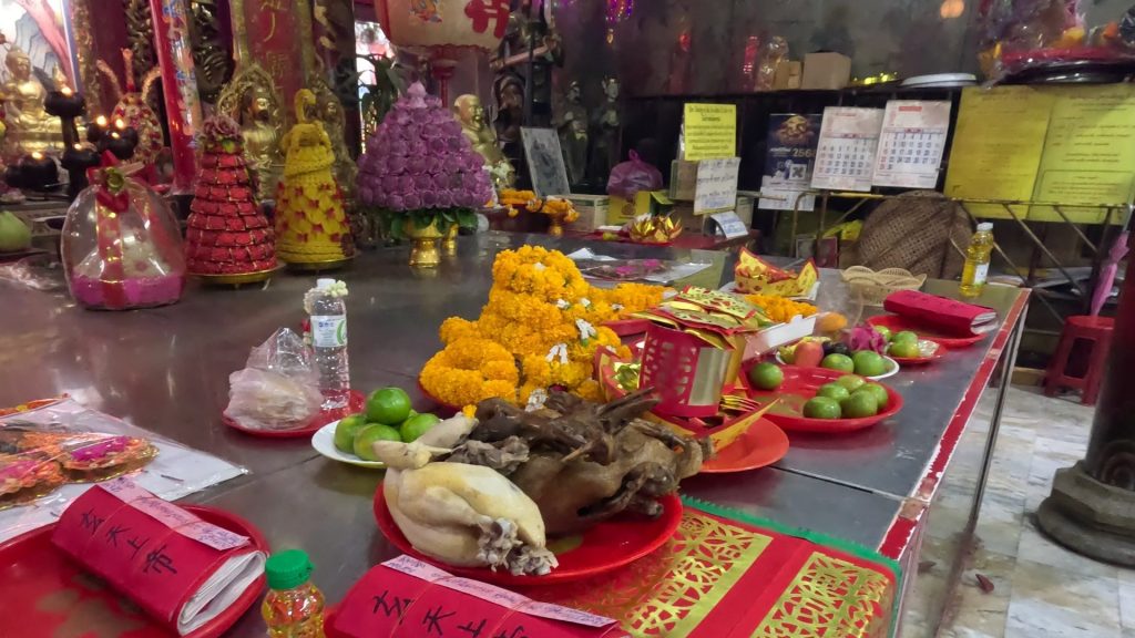 Bright yellow marigold garlands and food placed at the altar of San Chao Pho Suea, symbols of purity and merit-making in Thai-Chinese tradition.