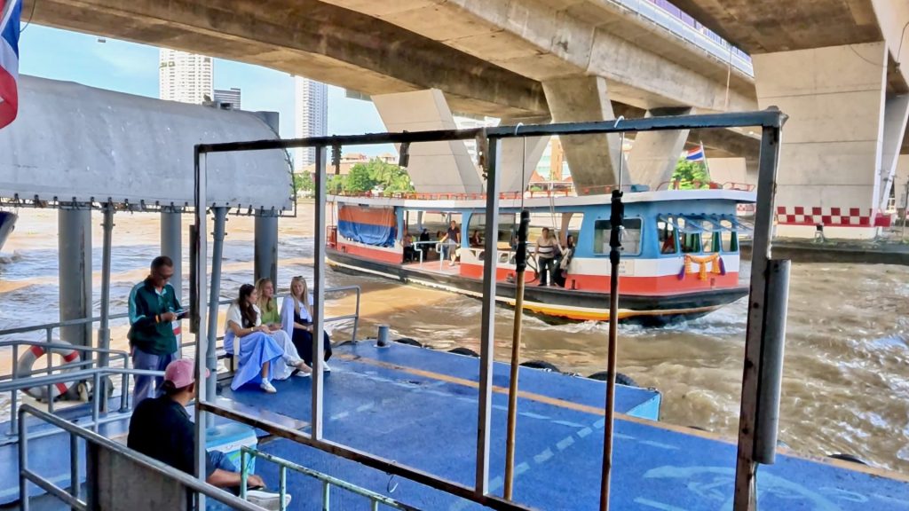 Ferry approaching Sathon Pier under Thaksin Bridge in Bangkok, with passengers waiting on the pier and the Chao Phraya River reflecting morning light.