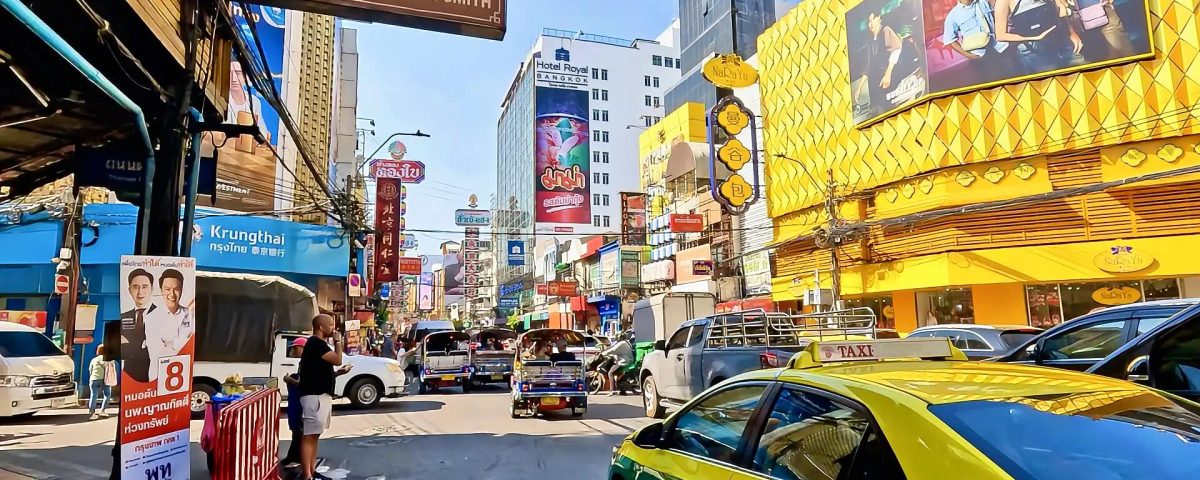 Busy traffic along Yaowarat Road in Bangkok Chinatown with colourful shop signs and buildings