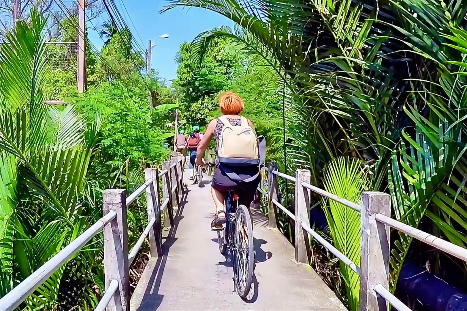 Cyclists riding along a narrow path through dense greenery in Bang Krachao, Bangkok