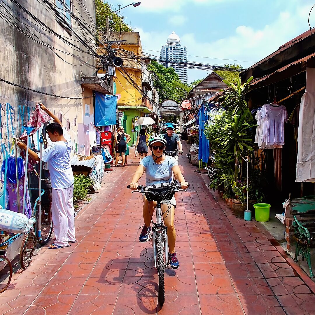 Bangkok bike tour cycling through small community street with resident hanging washing outside home