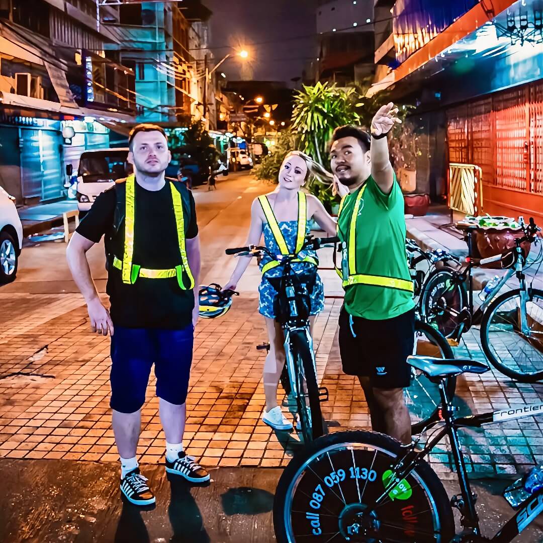 Bangkok night bike tour with guide explaining local area to visitors on a quiet street