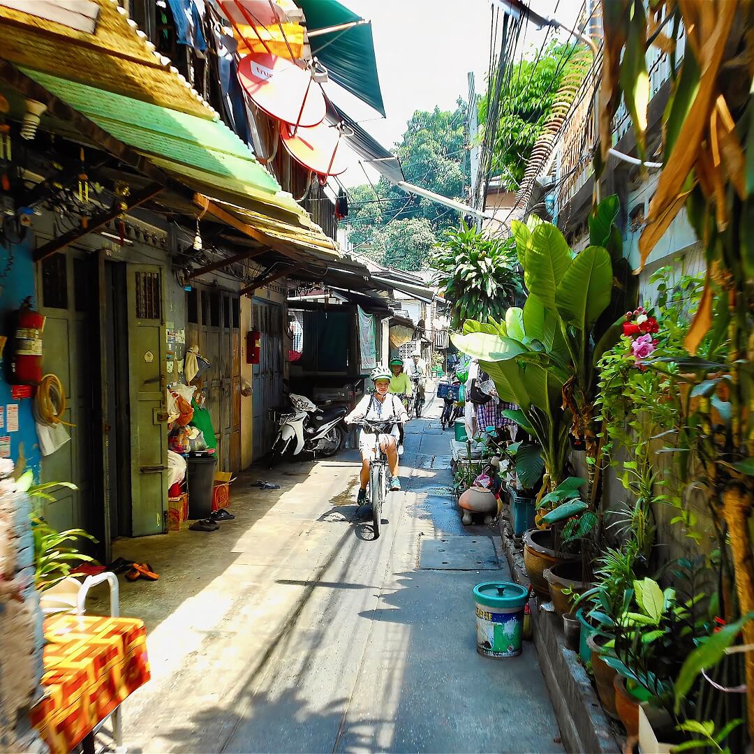 Small group Bangkok bike tour cycling through narrow neighbourhood street with shop houses