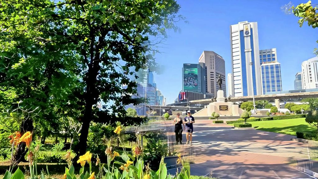 Cycling from Benjakitti Park to Lumphini Park showing elevated walkway with trees and flowers and joggers with city skyline in Bangkok