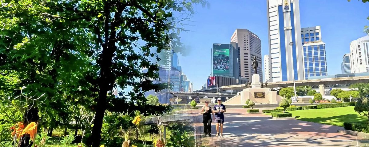 Cycling from Benjakitti Park to Lumphini Park showing elevated walkway with trees and flowers and joggers with city skyline in Bangkok