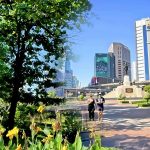 Cycling from Benjakitti Park to Lumphini Park showing elevated walkway with trees and flowers and joggers with city skyline in Bangkok