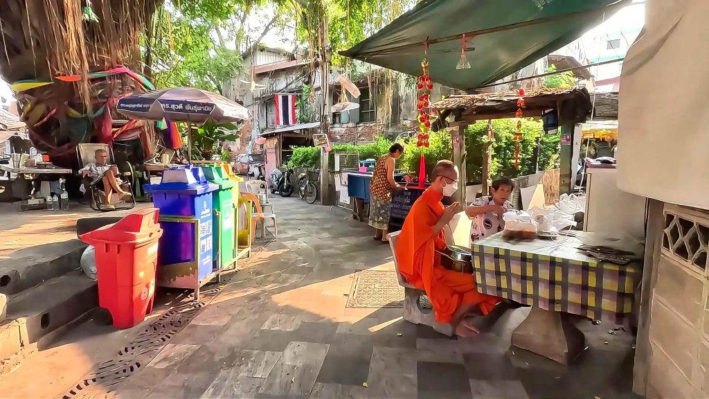 Monk sitting with local residents on a Talat Noi street in Bangkok in early morning sunlight