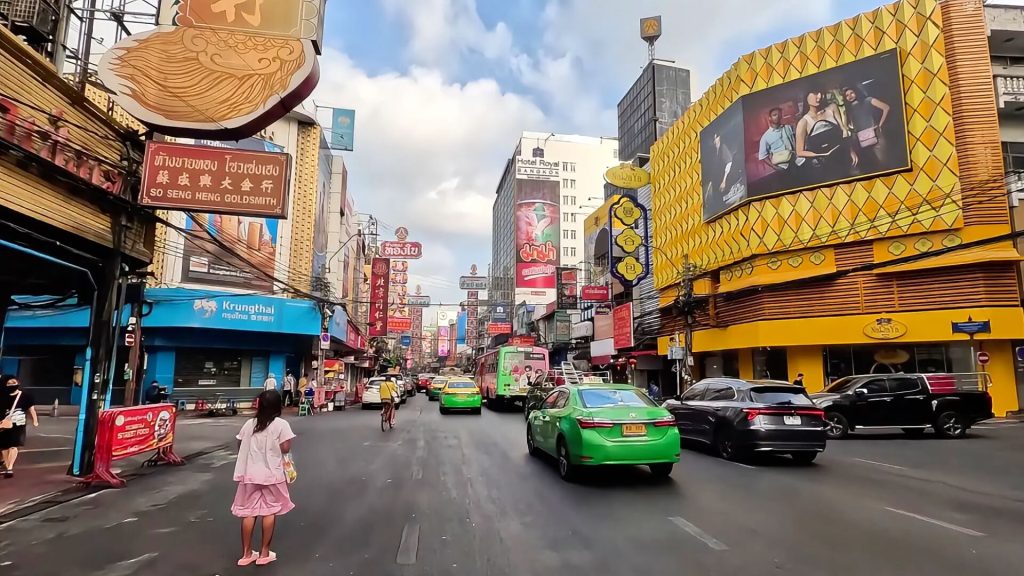 Busy early morning traffic on Yaowarat Road in Bangkok with colourful buildings and street signs